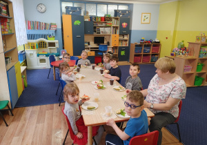 W klasie przy stolikach siedzą dzieci i wykonują kolorowe kanapki z różnych produktów.