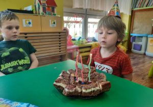 Chłopiec siedzi przed talerzem pełnym ciasta i zdmuchuje świeczki.