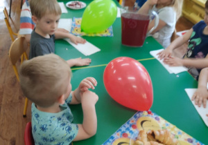 Dzieci siedzą przy stole i zjadają słodycze przyniesione i przygotowane przez mamę chłopca.