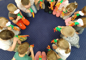 dzieci siedzą w kręgu na podłodze, dmuchają w kolorowe zabawki