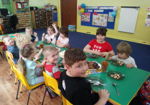 Dzieci siedzą przy stole i zajadają słodkości z okazji Dnia Dziecka.