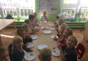 Dzieci przy stołach zjadają przygotowane knedle.