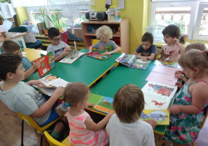 Dzieci siedzą przy stole i przeglądają z zainteresowaniem ksiązki.