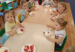 przy stolikach siedzą dzieci, jedzą lody z truskawkami