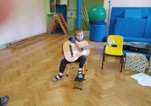 Chłopiec siedzi na krzesełku, trzyma gitarę