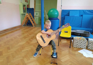Chłopiec siedzi na krzesełku, trzyma gitarę