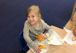 Dziewczynka siedzi przy stole i obiera mandarynkę.