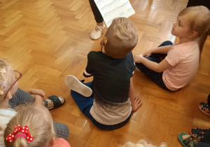 Dzieci siedzą na podłodze i oglądają zapis muzyczny utworu, którego wysłuchały.