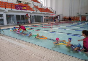 Dzieci w wodzie wraz z instruktorkami ustawiają się jeden za drugim.