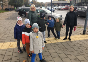 Dzieci stoją przed przejściem dla pieszych wraz z paniami.