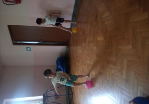 widok na salę gimnastyczną, z przodu chłopiec turla nogą piłkę, za nim chłopiec dotyka stopą piłkę