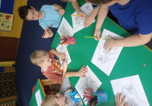 grupa dzieci siedzi przy stoliku i koloruje ilustrację