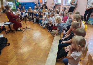 Przedszkolaki siedzą i słuchają koncertu muzycznego.