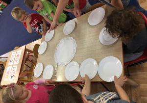 Dzieci stoją wokół stołu na którym rozstawione są talerzyki.