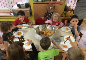 Dzieci siedzą przy stole i jedzą surówkę z kapusty przygotowaną własnoręcznie.