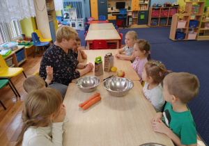 Dzieci siedzą przy stole i rozmawiają na temat składników surówki marchewkowej.