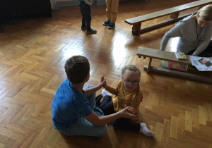 Chłopiec z dziewczynką siedzą na podłodze dotykając się dłońmi.
