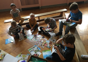 Dzieci siedzą na podłodze i wycinają z gazet ilustracje.