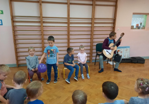 Uczeń wykonuje utwór na gitarze, a chłopiec prezentuje wiatr z wykorzystaniem balonika.