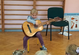 Dziewczynka prezentuje swoje umiejętności gry na gitarze.