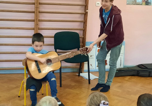 Chłopiec prezentuje swoje umiejętności gry na gitarze.