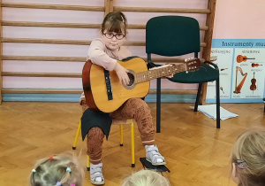 Dziewczynka prezentuje swoje umiejętności gry na gitarze.