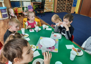Dzieci siedzą przy stole i zjadają słodkości i piją kompot.