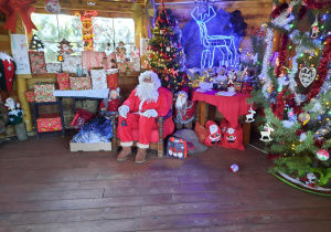 Na krześle obok choinki siedzi Święty Mikołaj.