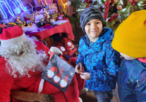Chłopiec uśmiecha się do obiektywu trzymając cukierka od Świętego Mikołaja.