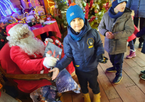 Chłopiec stoi obok Świętego Mikołaja i wskazuje prezenty.