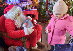 Dziewczynka z prezentem i cukierkiem odchodzi od Świętego Mikołaja.