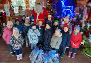 Dzieci z grupy IV pozują do zdjęcia ze Świętym Mikołajem i prezentami.