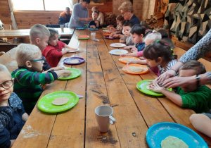 Dzieci siedzą przy stole i na talerzach ugniatają ciasto na pierniczki.