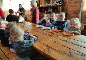 Dzieci siedzą przy stole i na talerzach ugniatają ciasto na pierniczki.