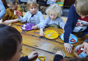 Dzieci siedzą przy stole i odciskają kształty w cieście.