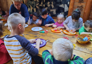 Dzieci siedzą przy stole i odciskają kształty w cieście.