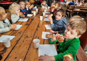 Dzieci siedzą przy stole i jedzą słodkie bułki popijając ciepłą herbatą.