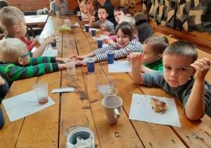 Dzieci siedzą przy stole i jedzą słodkie bułki popijając ciepłą herbatą.