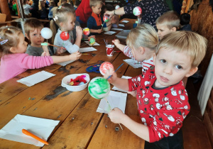 Dzieci siedzą przy stole i malują bombki.