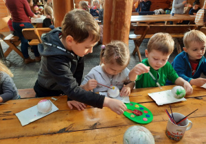 Dzieci siedzą przy stole i malują bombki.