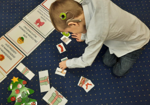 Chłopiec siedzi na dywanie i wybiera odpowiednie rysunki do zadania.