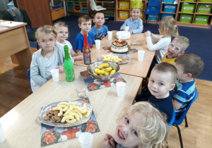 Dzieci siedzą wokół stołu na którym znajdują się słodycze.