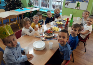 Dzieci siedzą wokół stołu na którym znajdują się słodycze.