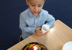Chłopiec siedzi przy stole przed tortem na którym płonie świeczka.