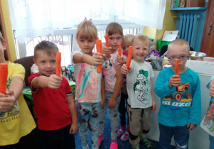 Dzieci trzymają w dłoniach marchewki.