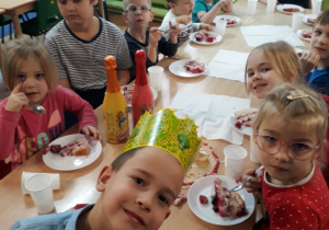 Dzieci siedzą przy stole i jedzą tort.