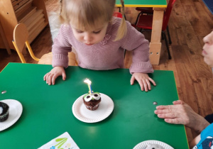 Dziewczynka dmucha świeczki umieszczone na babeczce.