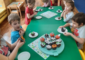 Dzieci siedzą przy stole i zjadają słodkie babeczki.