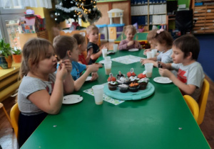 Dzieci siedzą przy stole i zjadają słodkie babeczki.