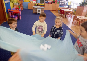 Dzieci podrzucają kule z papieru na materiale.